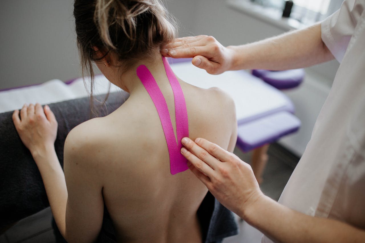 services-04 A healthcare professional applies kinesiology tape on a woman's neck for therapeutic treatment.